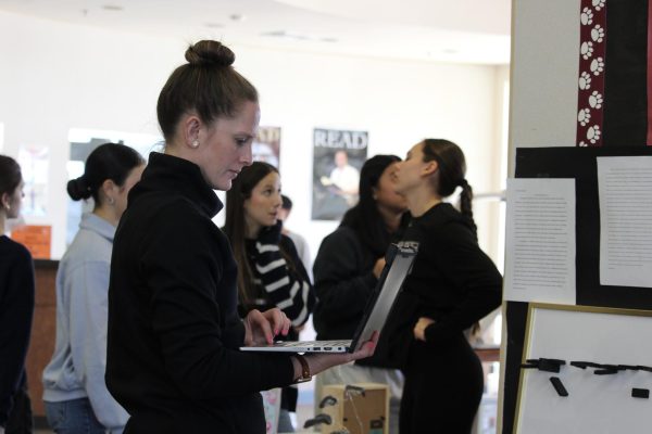 After assessing Gianna Dougherty’s project and reading her essay, Ms. Emilie Cavolt enters her grade into the gradebook. During the two days of the Truth Gallery projects being displayed in the library, Cavolt used her class times to grade all projects of AP Language Arts students Jan. 21-22. Photo by Sarah Choi.  