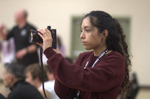 On the sidelines of the men’s varsity basketball game Feb. 12, Sayri Sanabria records the action as part of a video project. Photo by Paige Friesen